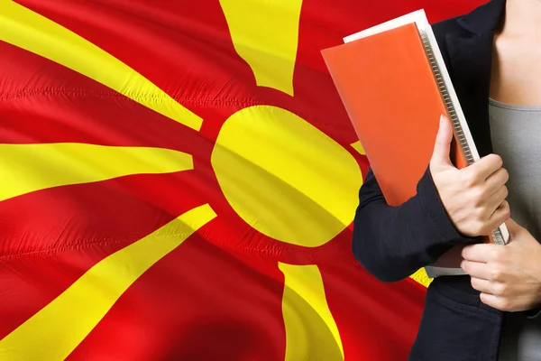 マケドニアの言語の概念を学習します 若い女性はバック グラウンドでマケドニアのフラグが立っています 先生の本 オレンジの空白ブック カバーを保持 — ストック写真