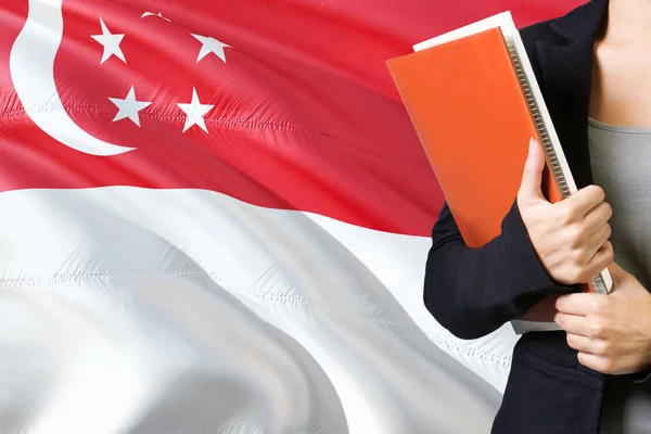 学习新加坡语概念 站在背景中的新加坡国旗的年轻女子 老师拿着书 橙色空白书封面 — 图库照片