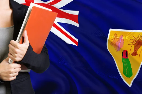 学习语言概念 年轻女子站在特克斯和凯科斯群岛 背景是国旗 老师拿着书 橙色空白书封面 — 图库照片