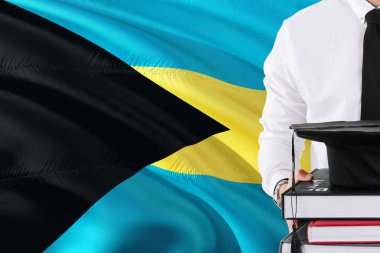 Başarılı Bahama öğrenci eğitim kavramı. Bahamalar bayrağı arka plan üzerinde tutan kitaplar ve mezuniyet kep.