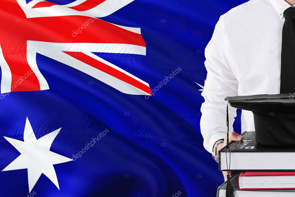 Successful Australian student education concept. Holding books and graduation cap over Australia flag background.