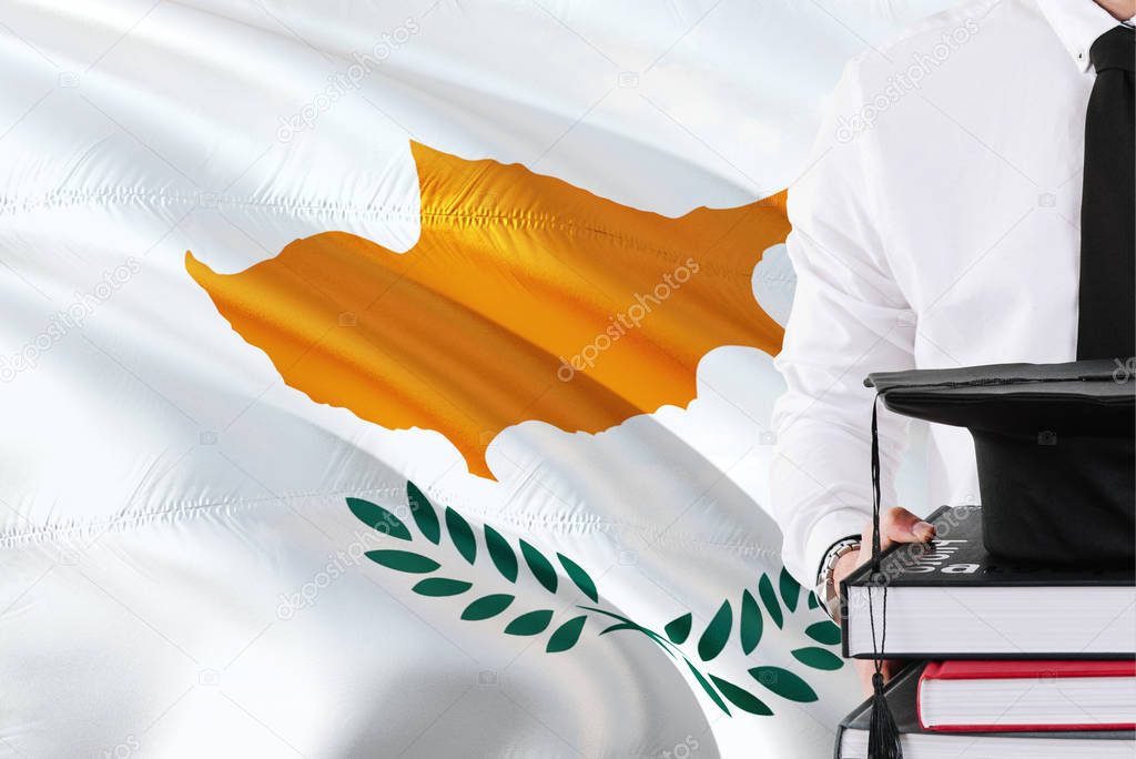 Successful Cypriot student education concept. Holding books and graduation cap over Cyprus flag background.