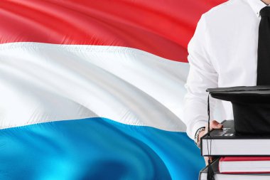 Başarılı Luxembourger öğrenci eğitim kavramı. Lüksemburg bayrağı arka plan üzerinde tutan kitaplar ve mezuniyet kep.