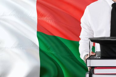 Başarılı Madagaskarlı öğrenci eğitim kavramı. Madagaskar bayrağı arka plan üzerinde tutan kitaplar ve mezuniyet kep.