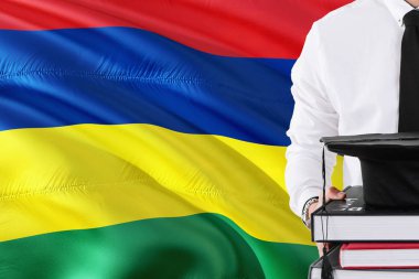 Başarılı Mauritian öğrenci eğitim kavramı. Mauritius bayrak arka plan üzerinde tutan kitaplar ve mezuniyet kep.
