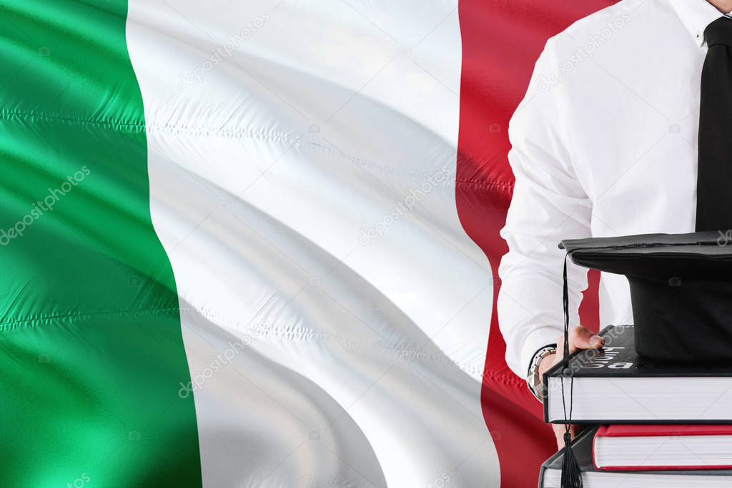 Successful Italian student education concept. Holding books and graduation cap over Italy flag background.