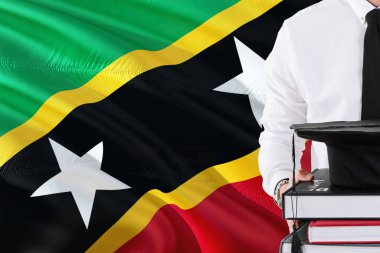 Başarılı öğrenci eğitim kavramı. Saint Kitts ve Nevis bayrak arka plan üzerinde tutan kitaplar ve mezuniyet kep.