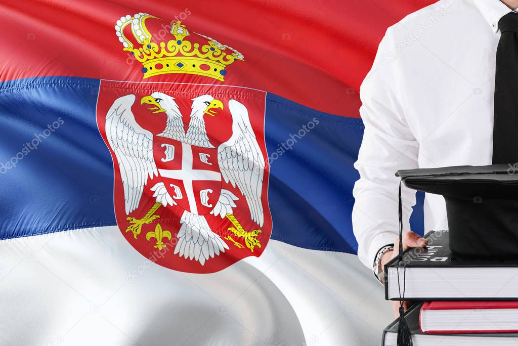 Successful Serbian student education concept. Holding books and graduation cap over Serbia flag background.