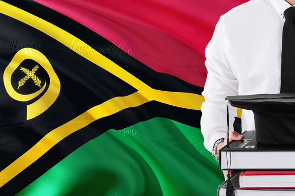Başarılı öğrenci eğitim kavramı. Vanuatu bayrağını arka plan üzerinde tutan kitaplar ve mezuniyet kep.