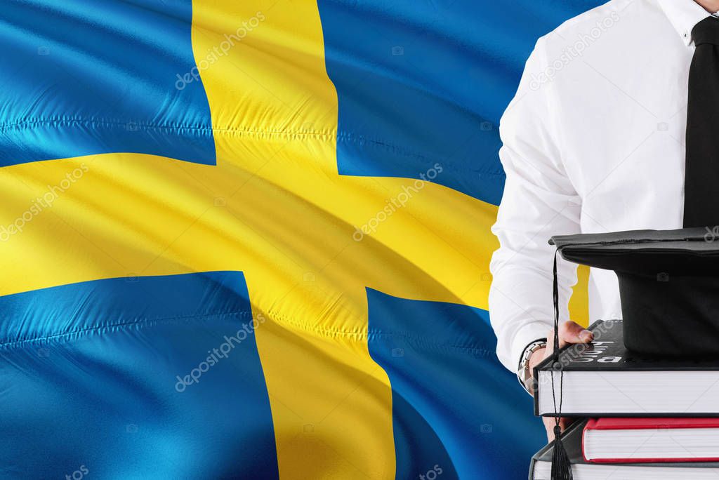 Successful Swedish student education concept. Holding books and graduation cap over Sweden flag background.