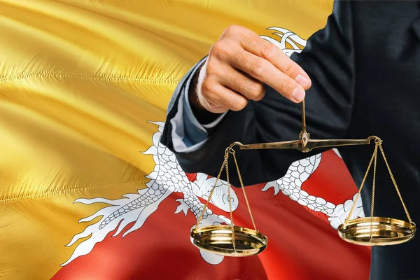 Bhutanese Judge is holding golden scales of justice with Bhutan waving flag background. Equality theme and legal concept.