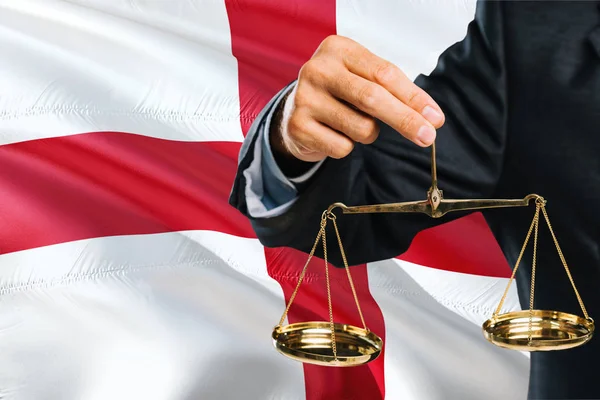 English Judge is holding golden scales of justice with England waving flag background. Equality theme and legal concept.