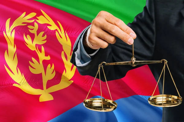 Eritrean Judge is holding golden scales of justice with Eritrea waving flag background. Equality theme and legal concept.