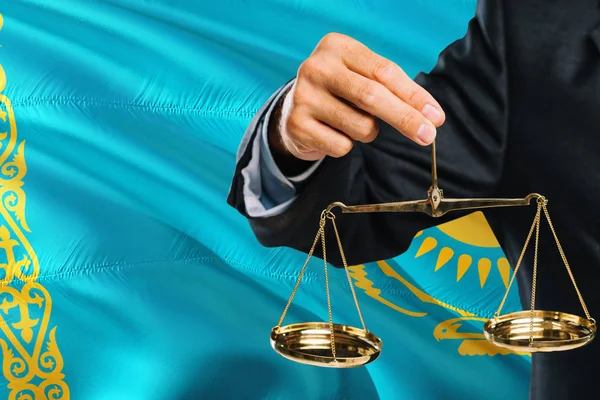 Kazakh Judge is holding golden scales of justice with Kazakhstan waving flag background. Equality theme and legal concept.
