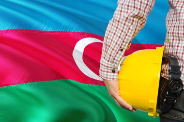 Mühendis sarı güvenlik kask sallayarak Azerbaycan bayrağı arka plan ile tutuyor. İnşaat ve yapı kavramı.