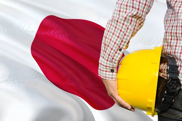 Japanese Engineer is holding yellow safety helmet with waving Japan flag background. Construction and building concept.