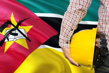 Mozambik mühendis sarı güvenlik kask sallayarak Mozambik bayrak arka plan ile tutuyor. İnşaat ve yapı kavramı.
