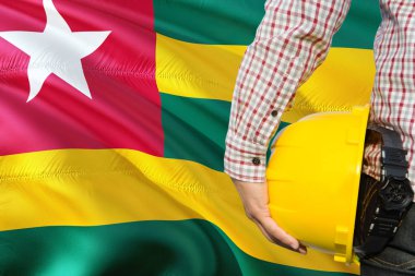 Togolu mühendis sarı güvenlik kask sallayarak Togo bayrak arka plan ile tutuyor. İnşaat ve yapı kavramı.
