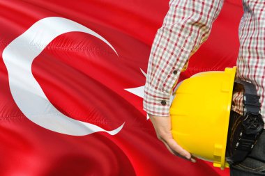 Türk Mühendis sarı güvenlik kask sallayarak Türkiye bayrağı arka plan ile tutuyor. İnşaat ve yapı kavramı.