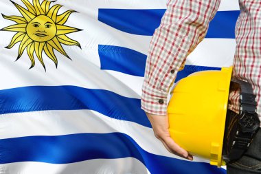 Uruguaylı mühendis sarı güvenlik kask sallayarak Uruguay bayrağı arka plan ile tutuyor. İnşaat ve yapı kavramı.