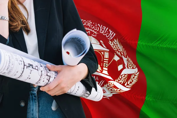 Afghan Architect woman holding blueprint against Afghanistan waving flag background. Construction and architecture concept.
