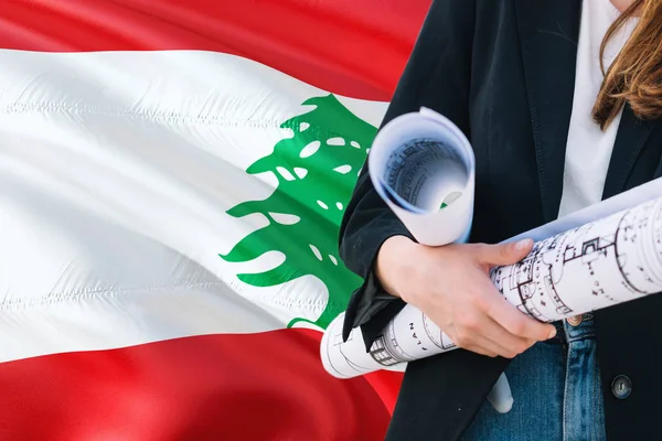 Lebanese Architect woman holding blueprint against Lebanon waving flag background. Construction and architecture concept.