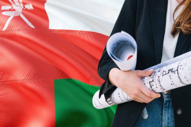 Omani Architect woman holding blueprint against Oman waving flag background. Construction and architecture concept. clipart