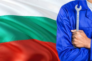 Mavi üniformalı Bulgar tamirci anahtarı sallayarak Bulgaristan bayrağı arka planı tutuyor. Çapraz silah teknisyen.