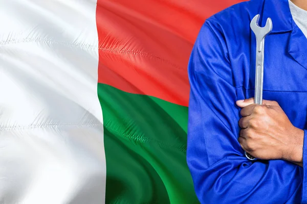 Mavi üniformalı Madagaskarlı tamirci anahtarı sallayarak Madagaskar bayrağı arka planı tutuyor. Çapraz silah teknisyen.