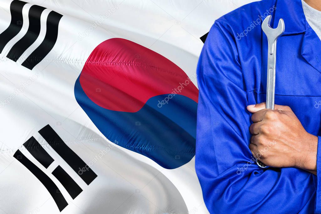 South Korean Mechanic in blue uniform is holding wrench against waving South Korea flag background. Crossed arms technician.