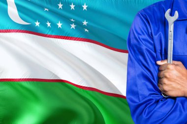 Mavi üniformalı özbek tamirci anahtarı sallayarak Özbekistan bayrağı arka planı tutuyor. Çapraz silah teknisyen.