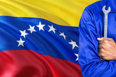 Mavi üniformalı Venezuela tamirci anahtarı sallayarak Venezuela bayrak arka planı tutuyor. Çapraz silah teknisyen.