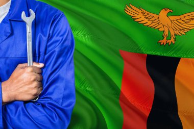 Mavi üniformalı Zambia tamirci anahtarı sallayarak Zambiya bayrağı arka planı tutuyor. Çapraz silah teknisyen.