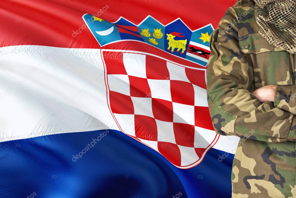 Crossed arms Croatian soldier with national waving flag on background - Croatia Military theme.