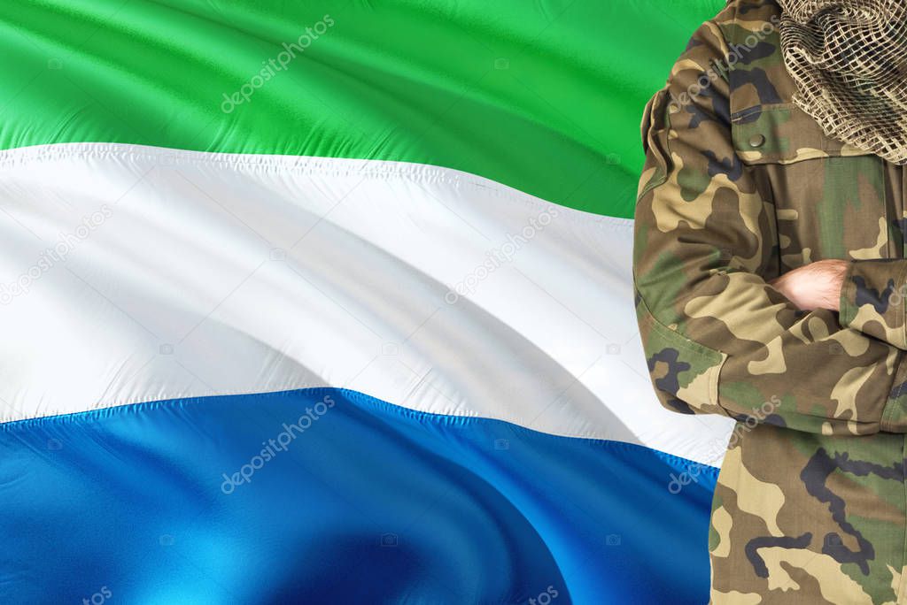 Crossed arms soldier with national waving flag on background - Sierra Leone Military theme.