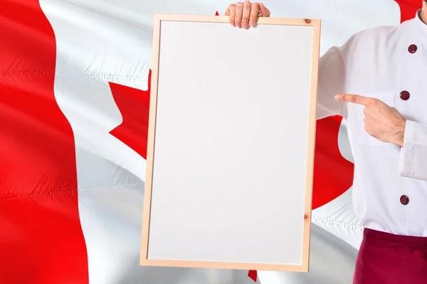 Canadian Chef holding blank whiteboard menu on Canada flag background. Cook wearing uniform pointing space for text.