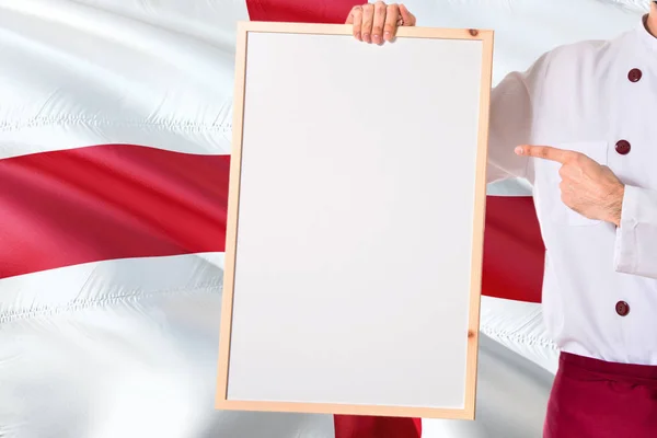 English Chef holding blank whiteboard menu on England flag background. Cook wearing uniform pointing space for text.