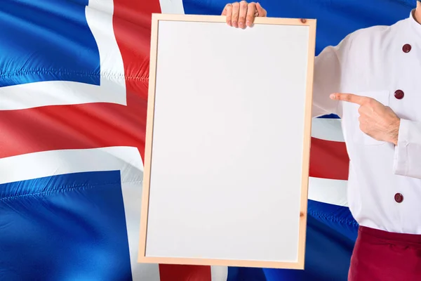 アイスランドの旗の背景の空白のホワイト ボード メニューを保持しているシェフ 本文制服ポインティング領域を着て調理します — ストック写真