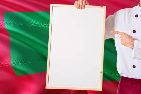 马尔代夫国旗背景上的马尔迪文厨师拿着空白白板菜单 烹饪穿着统一的指向空间的文字 — 图库照片