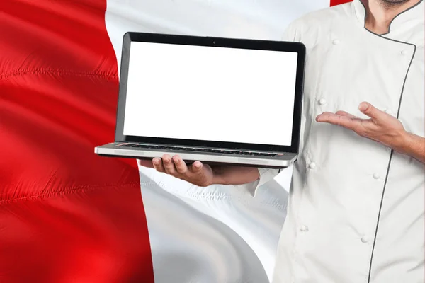 Peruvian Chef holding laptop with blank screen on Peru flag background. Cook wearing uniform and pointing laptop for copy space.