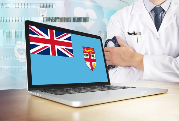 Fiji healthcare system in tech theme. Fijian flag on computer screen. Doctor standing with stethoscope in hospital. Cryptocurrency and Blockchain concept.