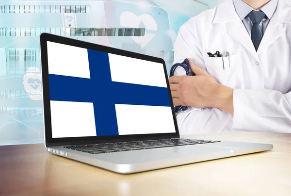 Finland healthcare system in tech theme. Finnish flag on computer screen. Doctor standing with stethoscope in hospital. Cryptocurrency and Blockchain concept.