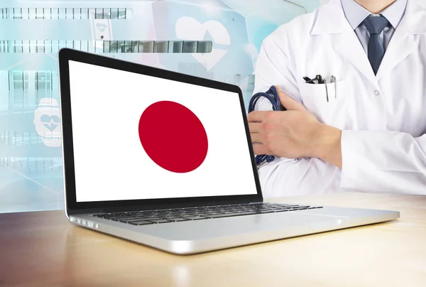 Japan healthcare system in tech theme. Japanese flag on computer screen. Doctor standing with stethoscope in hospital. Cryptocurrency and Blockchain concept.