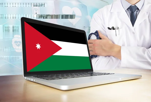 Jordan healthcare system in tech theme. Jordanian flag on computer screen. Doctor standing with stethoscope in hospital. Cryptocurrency and Blockchain concept.