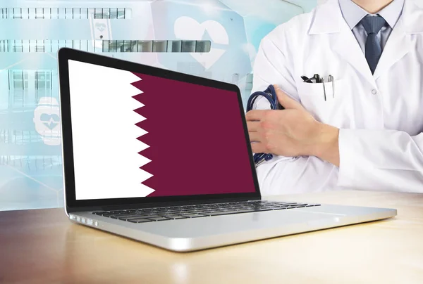 Qatar healthcare system in tech theme. Qatari flag on computer screen. Doctor standing with stethoscope in hospital. Cryptocurrency and Blockchain concept.
