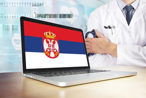 Serbia healthcare system in tech theme. Serbian flag on computer screen. Doctor standing with stethoscope in hospital. Cryptocurrency and Blockchain concept.