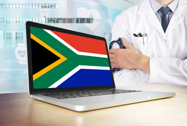 South Africa healthcare system in tech theme. South African flag on computer screen. Doctor standing with stethoscope in hospital. Cryptocurrency and Blockchain concept.