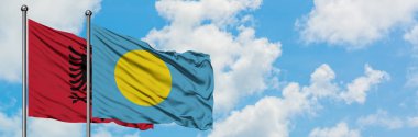 Arnavutluk ve Palau bayrağı birlikte beyaz bulutlu mavi gökyüzüne karşı rüzgarda sallayarak. Diplomasi kavramı, uluslararası ilişkiler.