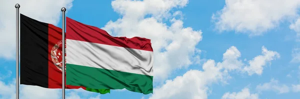 Bandera de Afganistán y Hungría ondeando en el viento contra el cielo azul nublado blanco juntos. Concepto diplomático, relaciones internacionales . — Foto de Stock