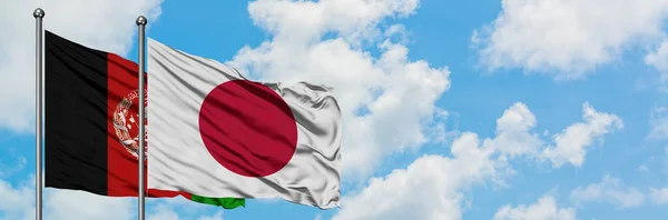 Bandera de Afganistán y Japón ondeando en el viento contra el cielo azul nublado blanco juntos. Concepto diplomático, relaciones internacionales . — Foto de Stock